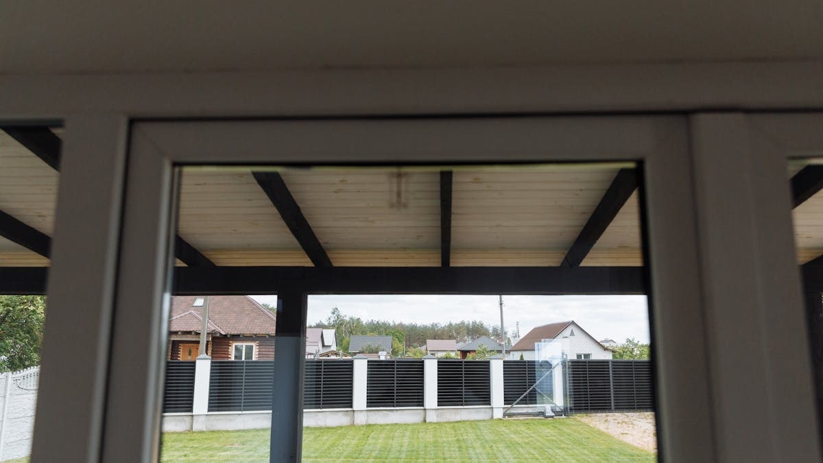 A view through a window overlooking a tidy suburban backyard with green grass.