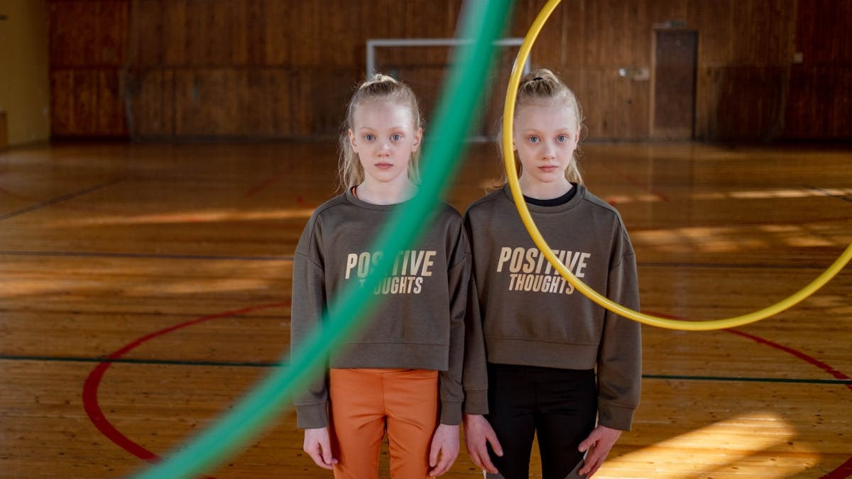 Twins stand indoors with hula hoops, promoting positive thoughts and teamwork.